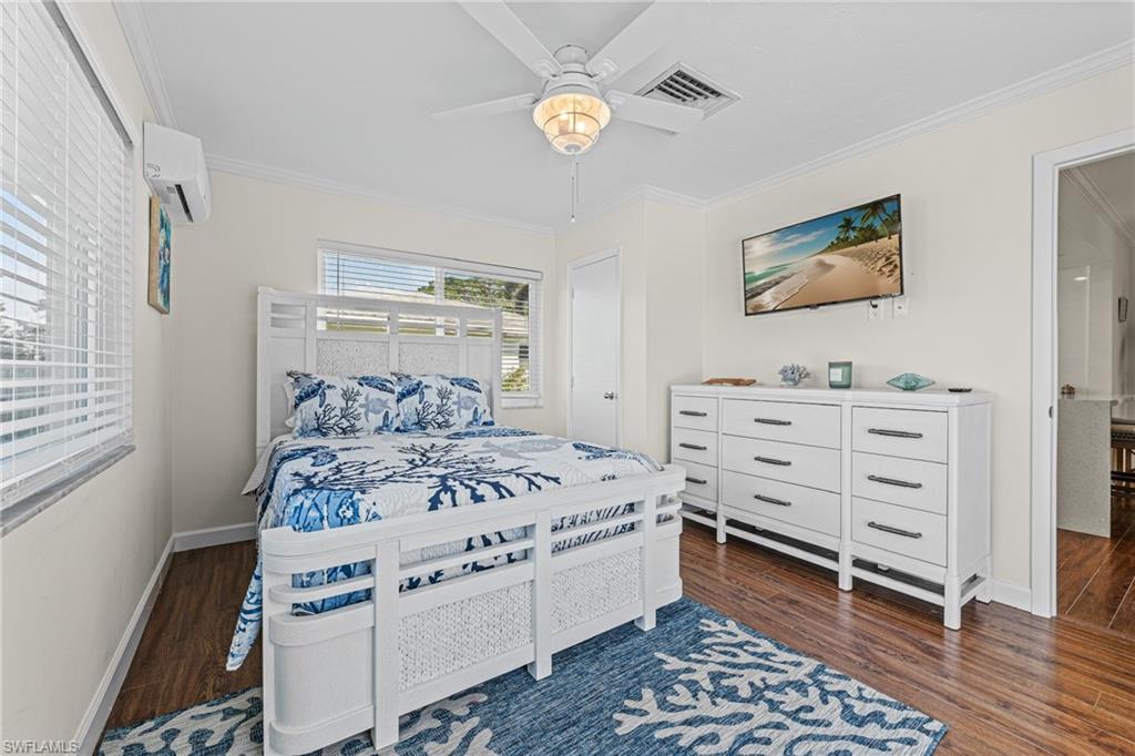 Bedroom with ornamental molding, wood finished floors, a wall mounted air conditioner, and ceiling fan