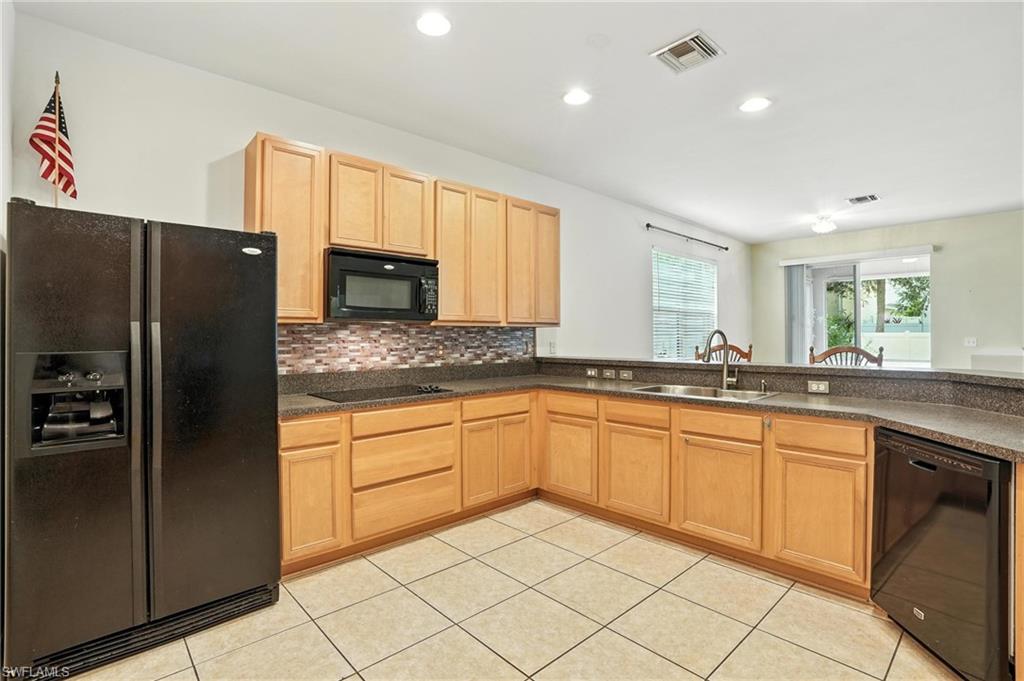 Kitchen featuring black appliances, light brown cabinetry, light tile patterned floors, dark countertops, and recessed lighting