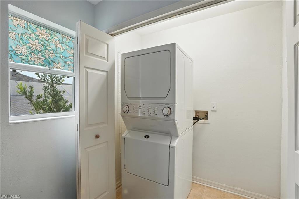 Laundry area with stacked washer / drying machine and light tile patterned flooring