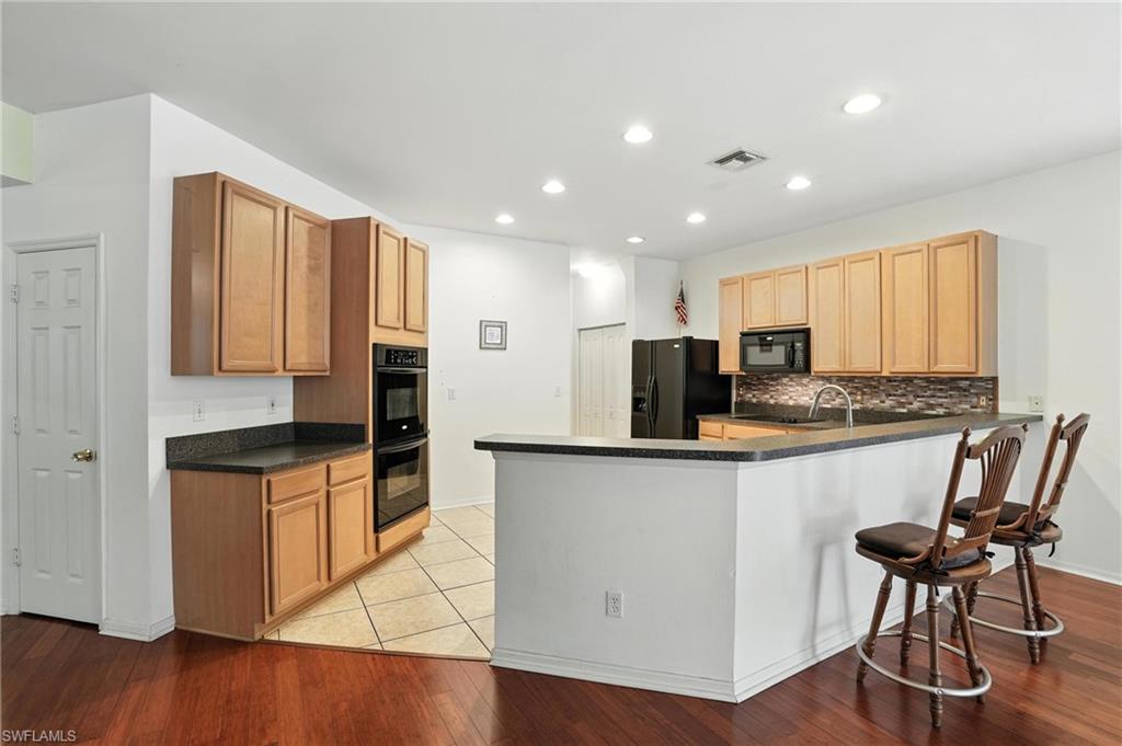 Kitchen with black appliances, a peninsula, dark countertops, tasteful backsplash, and light wood-type flooring