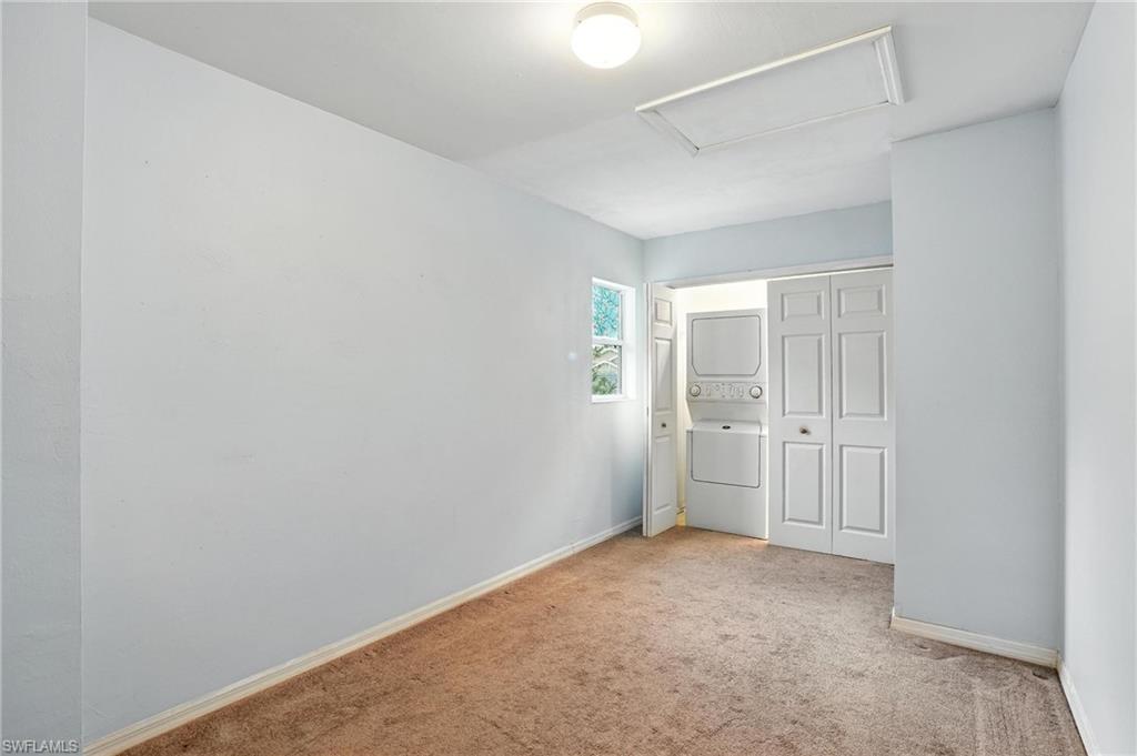 Unfurnished bedroom featuring stacked washing machine and dryer and carpet flooring
