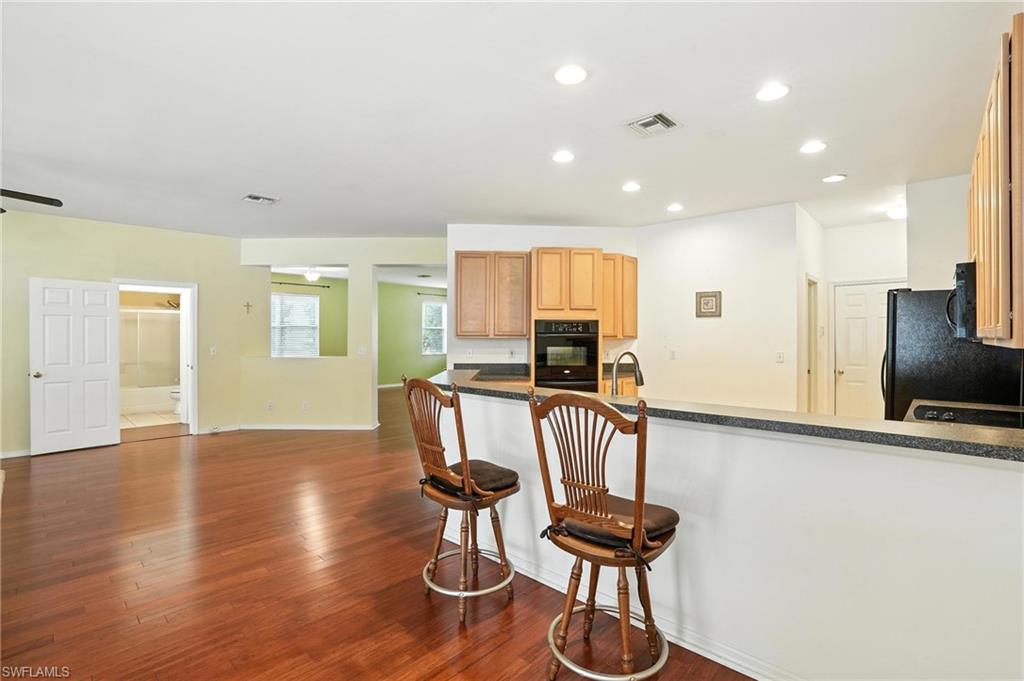 Kitchen with black appliances, wood finished floors, dark countertops, a breakfast bar, and recessed lighting