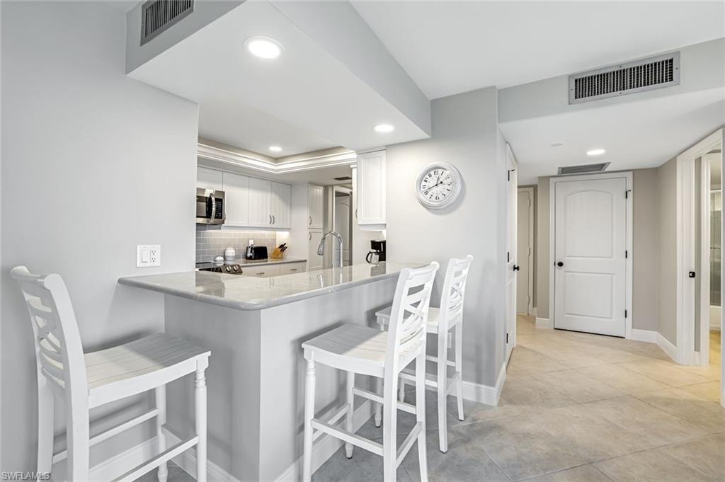 Kitchen featuring stainless steel microwave, recessed lighting, white cabinets, a breakfast bar area, and tasteful backsplash