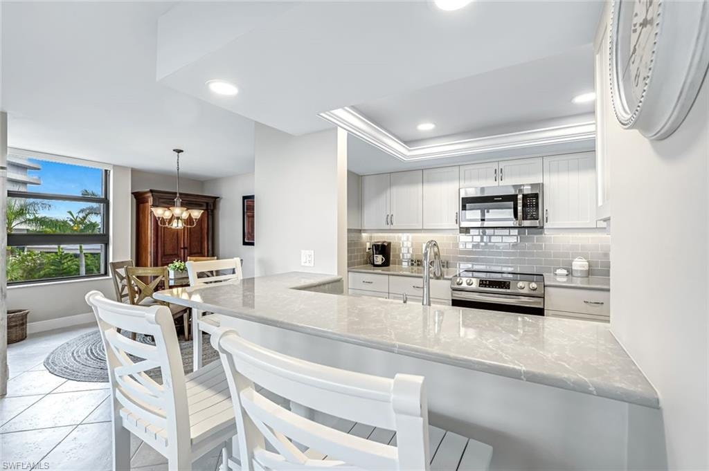 Kitchen with stainless steel appliances, tasteful backsplash, white cabinetry, a chandelier, and light stone countertops