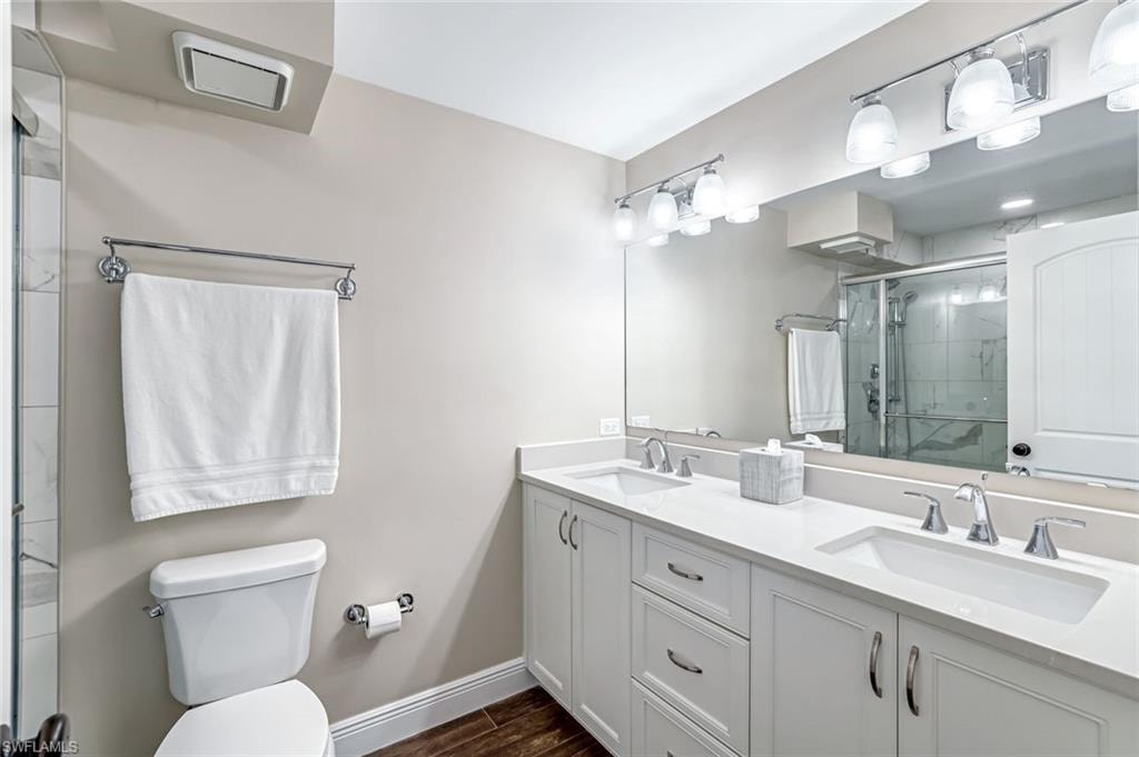 Full bath with double vanity, a stall shower, and wood finished floors