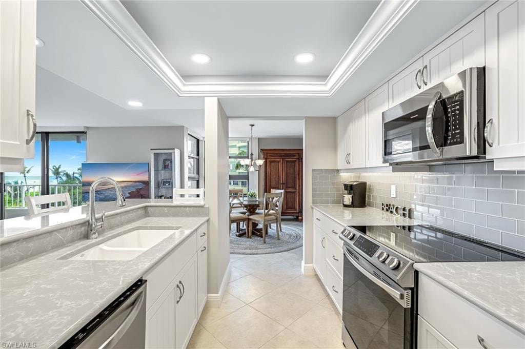 Kitchen featuring stainless steel appliances, decorative backsplash, white cabinetry, a tray ceiling, and recessed lighting