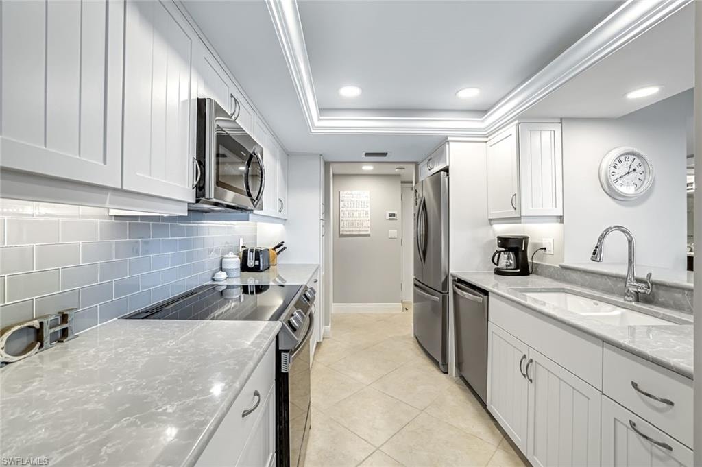 Kitchen featuring appliances with stainless steel finishes, decorative backsplash, a tray ceiling, white cabinets, and light stone countertops