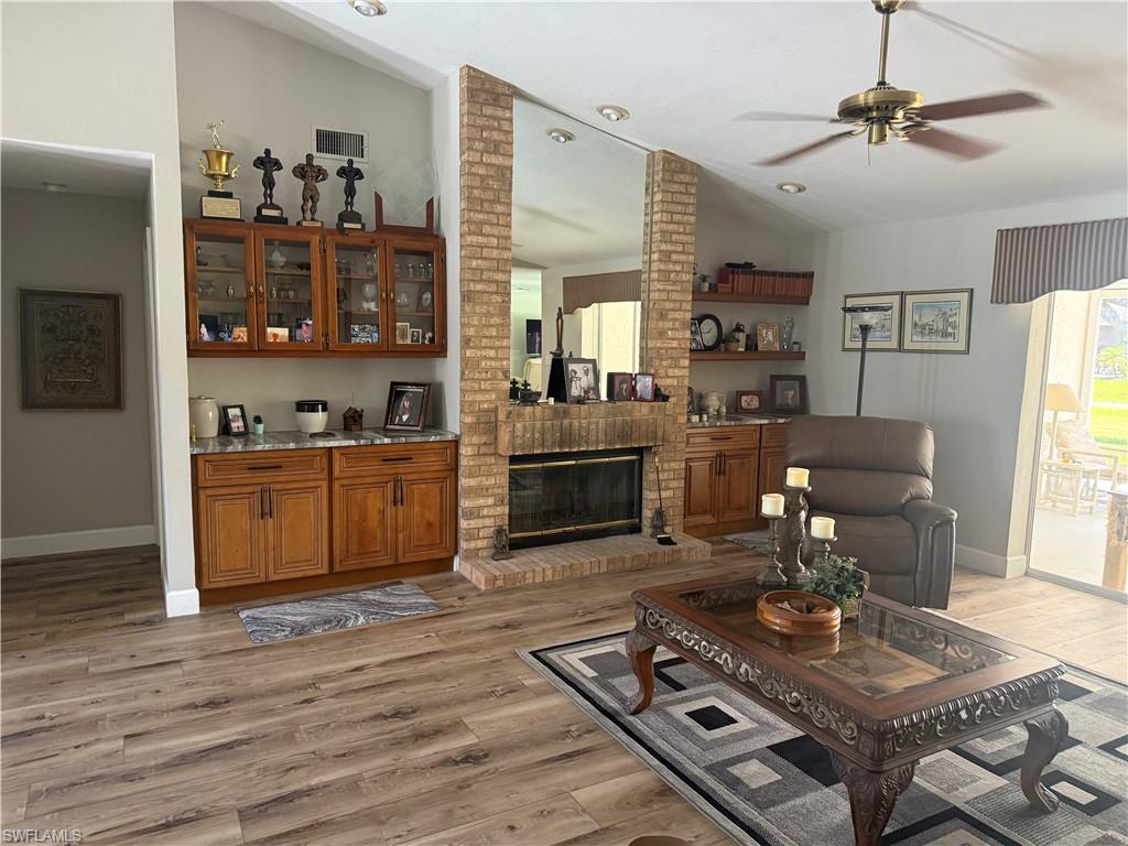 Living room featuring vaulted ceiling, light wood-type flooring, ceiling fan, and a fireplace