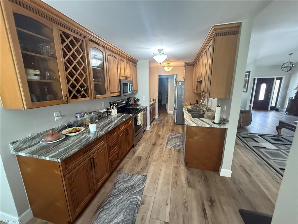 Kitchen featuring appliances with stainless steel finishes, glass insert cabinets, light wood-type flooring, and stone countertops