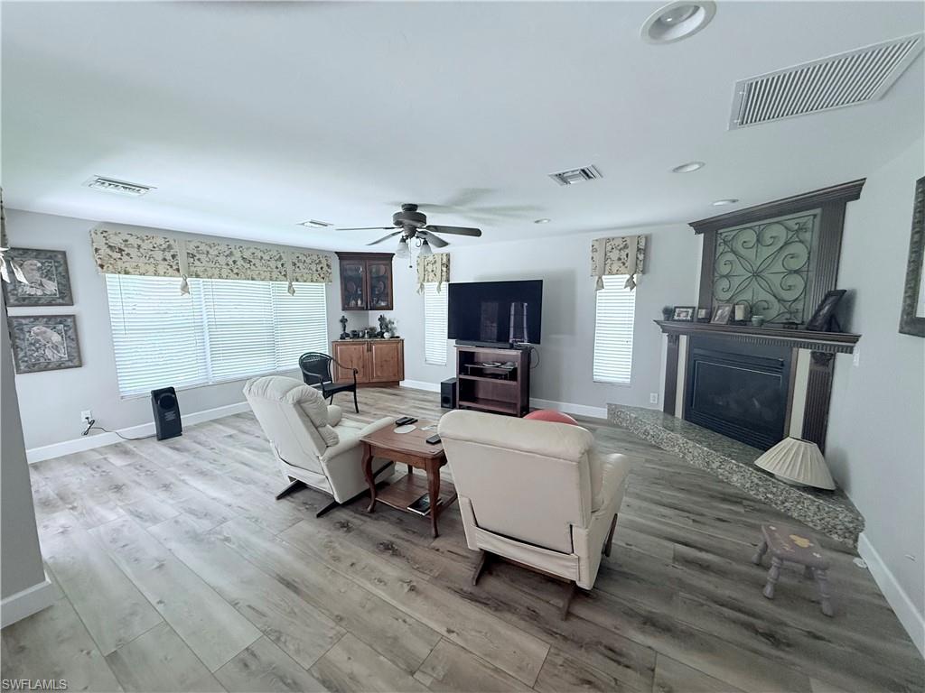 Living area with wood finished floors, a fireplace with raised hearth, a ceiling fan, and recessed lighting