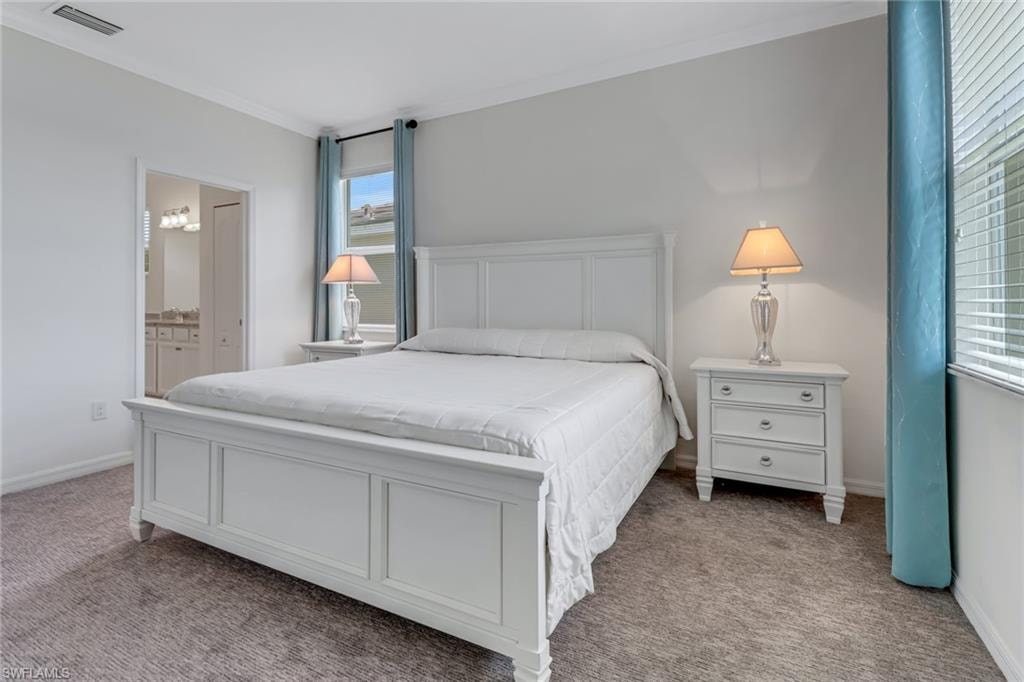Primary Bedroom with carpet, multiple windows, ensuite bath, and crown molding