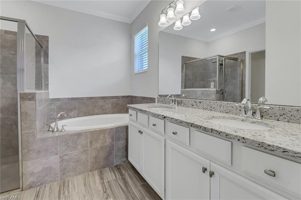 Primary Bathroom featuring a shower stall, double vanity, a bath, and ornamental molding
