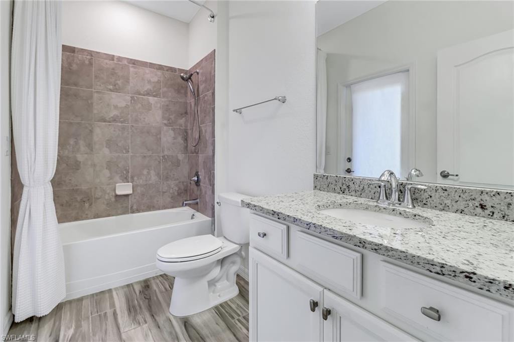 Full bath featuring shower / bath combo with shower curtain, vanity, and wood finished floors