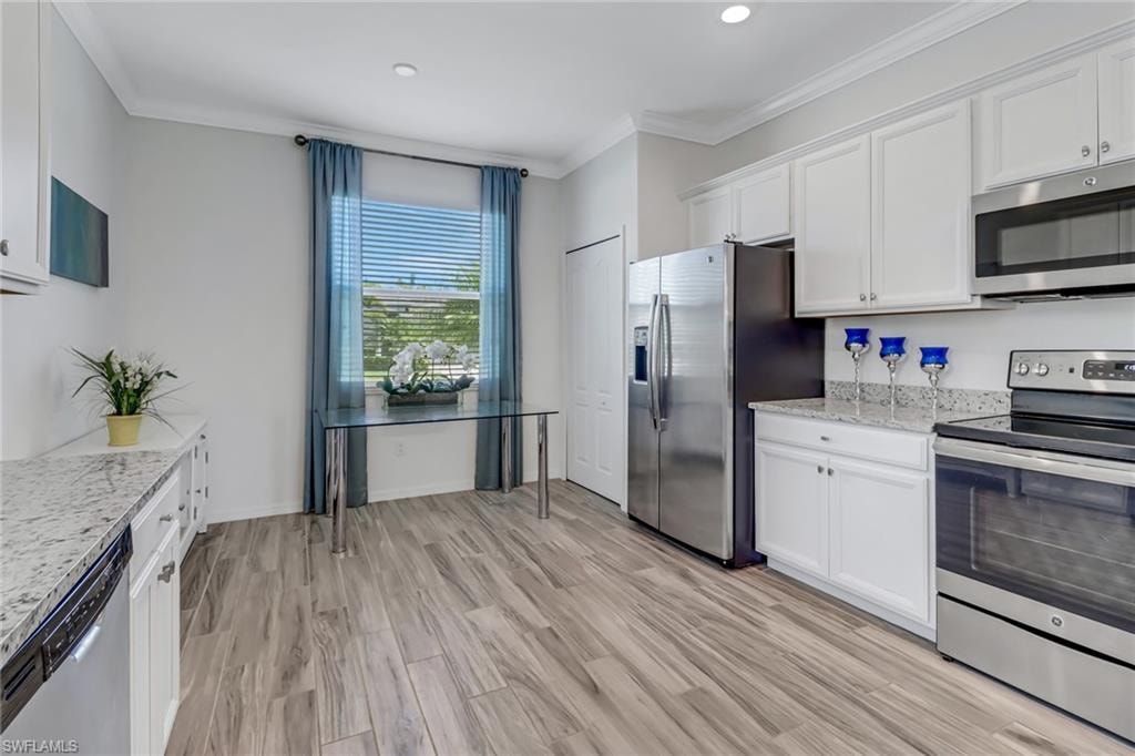 Kitchen featuring stainless steel appliances, ornamental molding, white cabinetry, light stone counters, and light wood finished floors