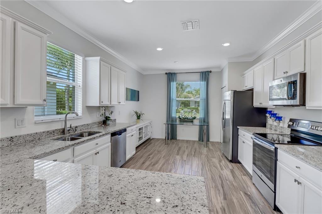 Kitchen featuring appliances with stainless steel finishes, white cabinetry, light wood finished floors, crown molding, and recessed lighting