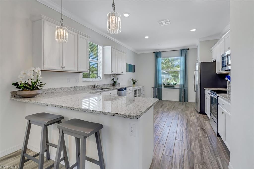 Kitchen featuring stainless steel appliances, crown molding, white cabinets, a peninsula, and a kitchen bar