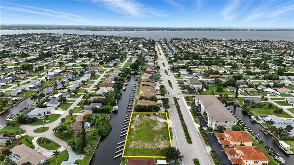 Aerial view of property and surrounding area featuring a large body of water, property parcel outlined, and nearby suburban area