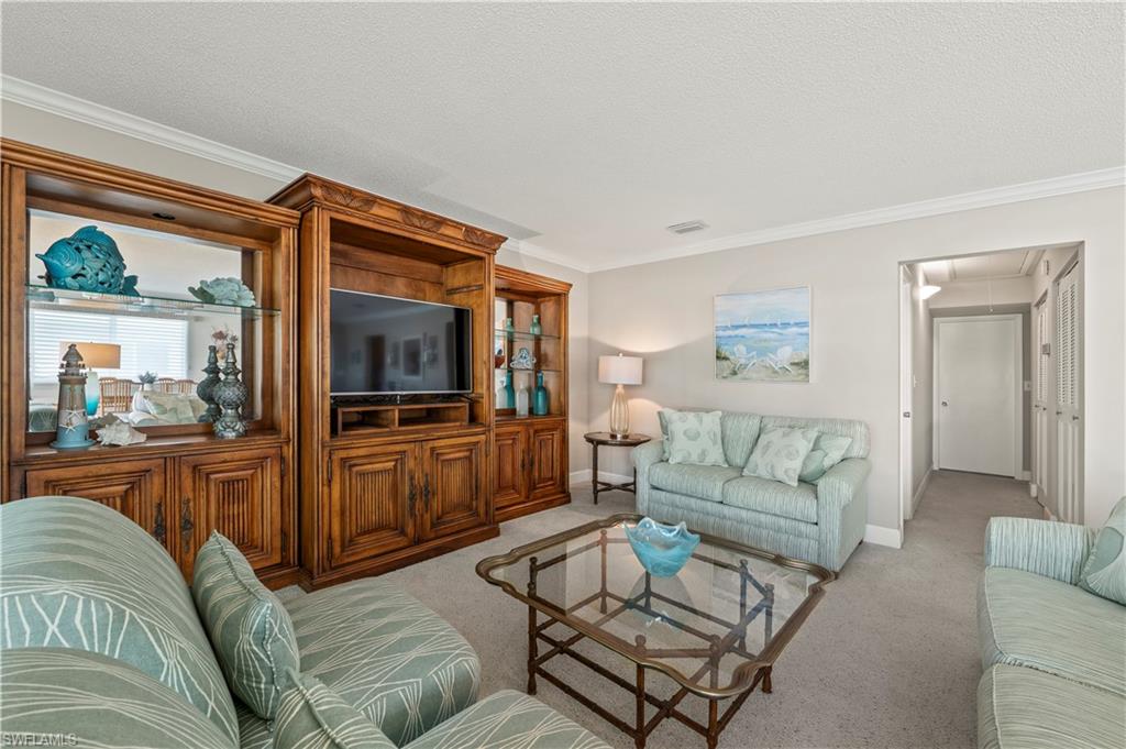 Living room with attic access, light colored carpet, crown molding, and a textured ceiling