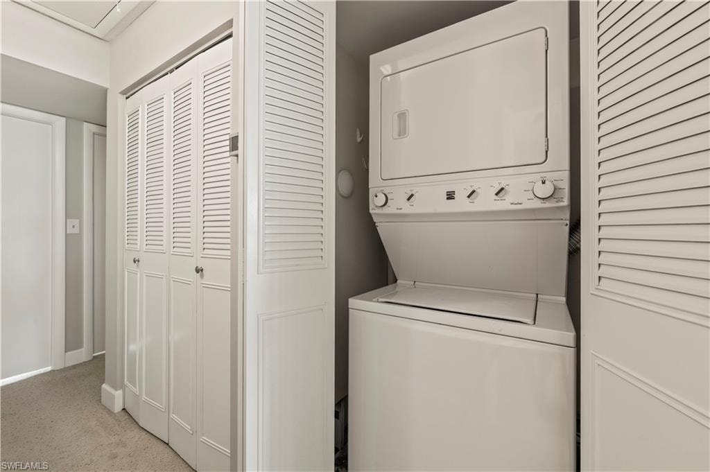 Washroom with stacked washer and clothes dryer and light colored carpet