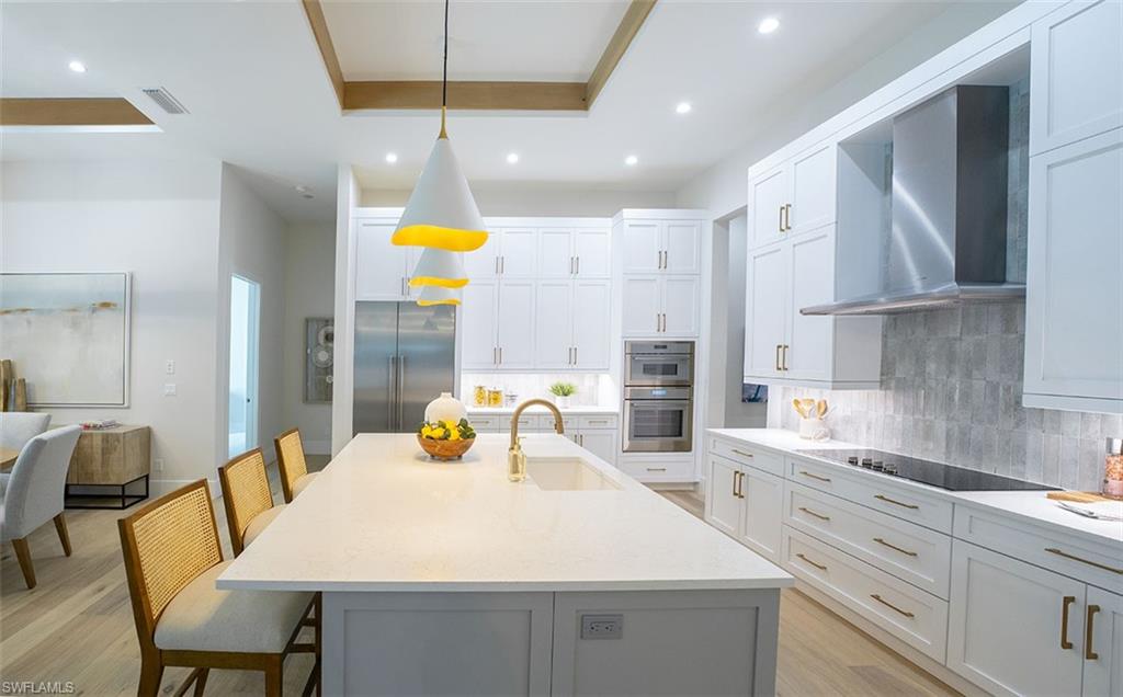 Kitchen with wall chimney exhaust hood, a kitchen breakfast bar, pendant lighting, tasteful backsplash, and recessed lighting