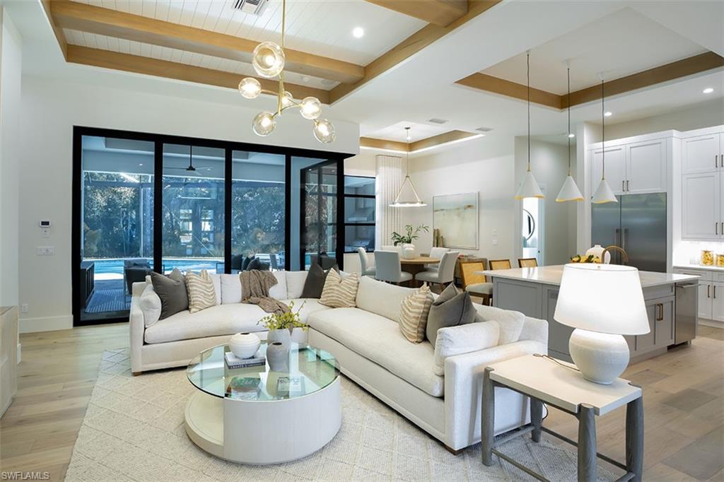 Living area with light wood-style flooring, a raised ceiling, a chandelier, beamed ceiling, and recessed lighting