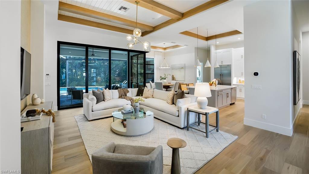 Living area with a chandelier, beamed ceiling, light wood-type flooring, and a raised ceiling