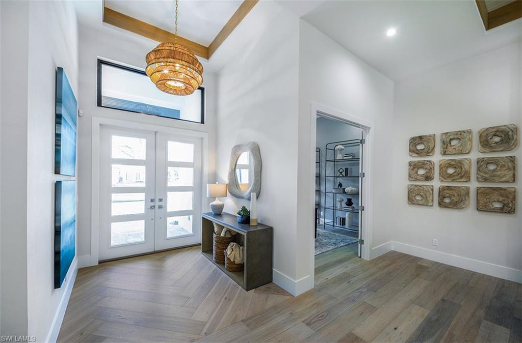 Foyer entrance with french doors, a towering ceiling, a chandelier, and parquet flooring
