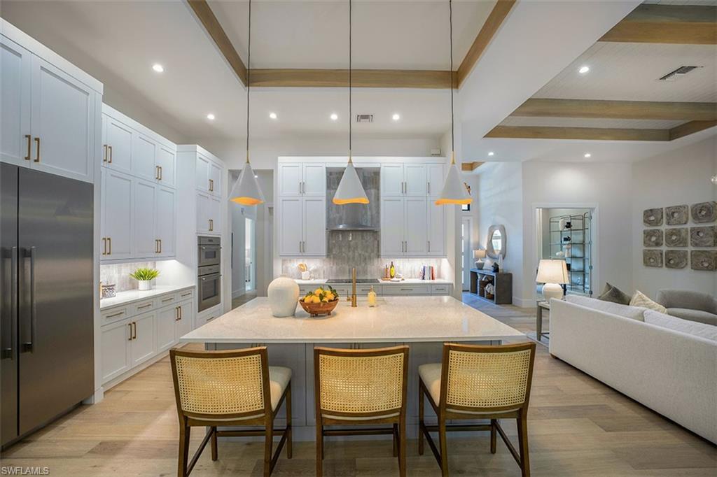 Kitchen with appliances with stainless steel finishes, open floor plan, a kitchen bar, light wood-type flooring, and beamed ceiling