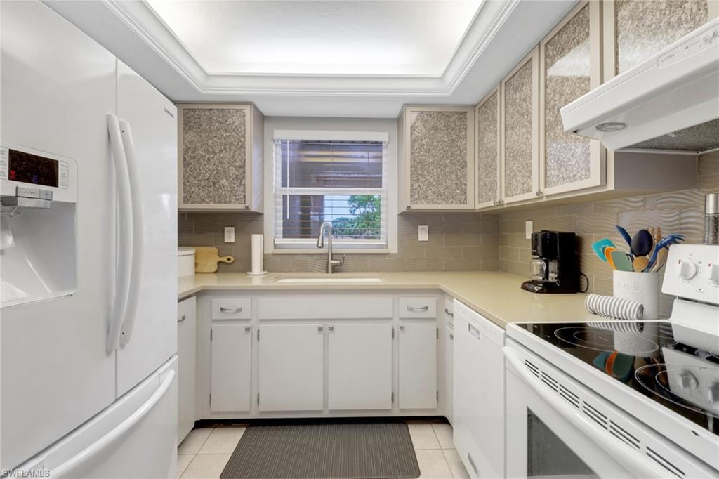 Kitchen with white appliances, extractor fan, light tile patterned floors, tasteful backsplash, and light countertops
