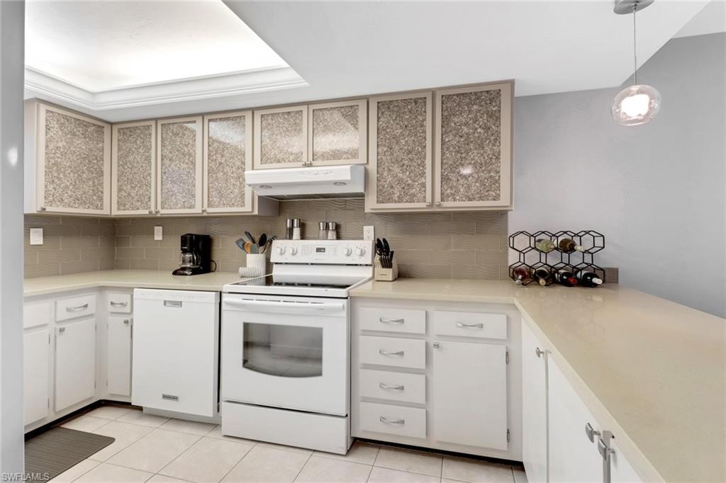 Kitchen featuring white appliances, under cabinet range hood, decorative backsplash, light tile patterned flooring, and light countertops