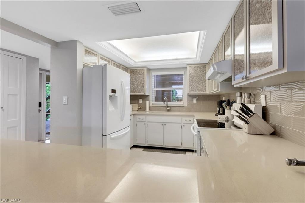 Kitchen featuring white appliances, under cabinet range hood, tasteful backsplash, and light countertops
