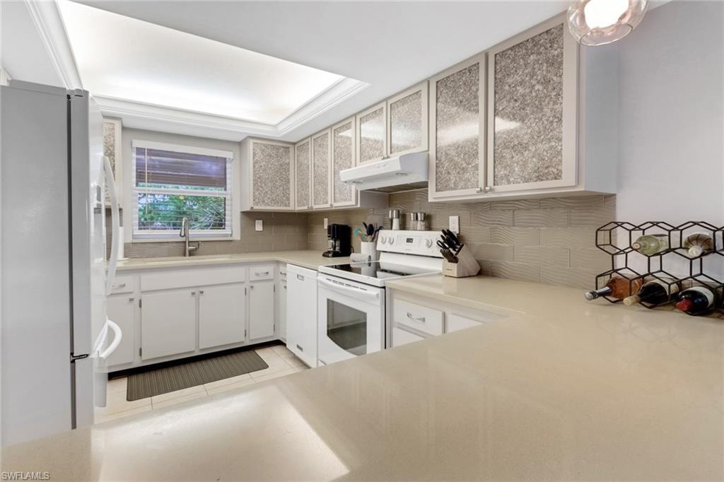 Kitchen featuring white appliances, under cabinet range hood, decorative backsplash, and light countertops