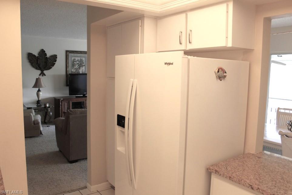 Kitchen featuring white refrigerator with ice dispenser, white cabinetry, light carpet, and light stone countertops