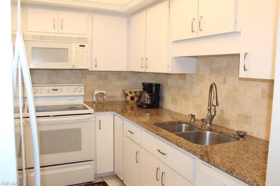 Kitchen featuring white appliances, tasteful backsplash, and white cabinetry