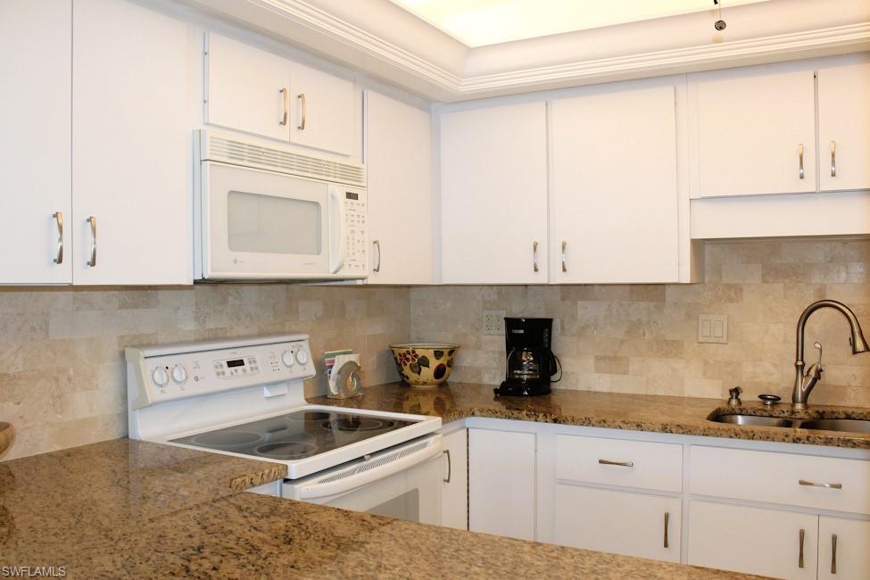 Kitchen with white appliances, white cabinetry, and decorative backsplash