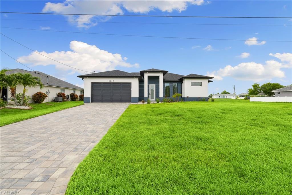 Prairie-style house featuring stucco siding, decorative driveway, a garage, and a front yard