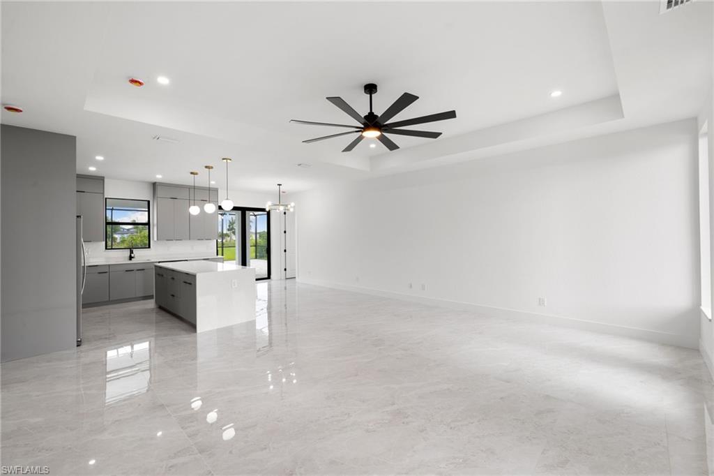 Unfurnished living room with a tray ceiling, ceiling fan, recessed lighting, and a chandelier