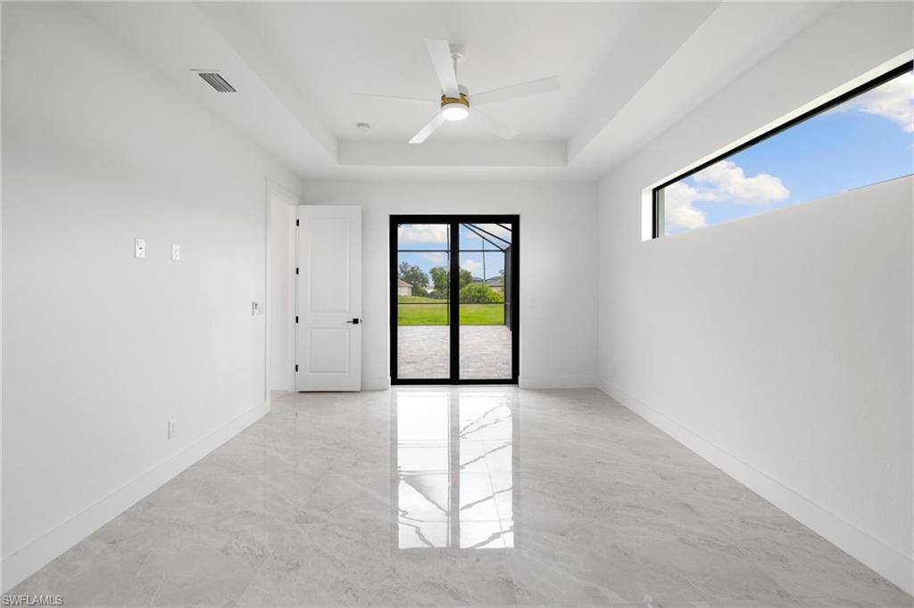 Spare room with a raised ceiling, a ceiling fan, and light marble finish floors
