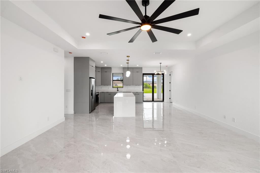 Unfurnished living room with a raised ceiling, recessed lighting, light marble finish flooring, ceiling fan, and a chandelier