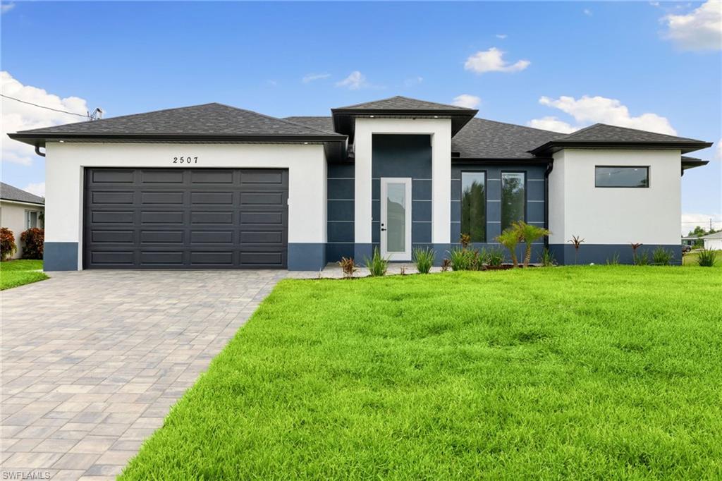 Prairie-style home featuring stucco siding, a front lawn, decorative driveway, and an attached garage