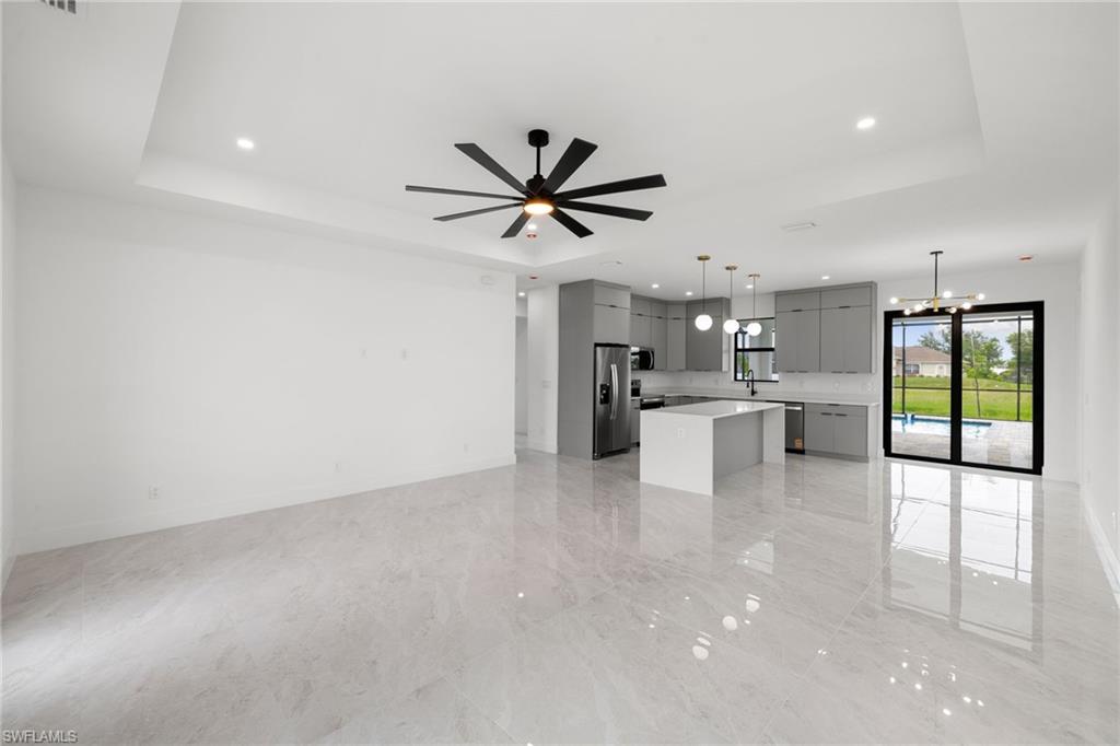 Unfurnished living room with a raised ceiling, a ceiling fan, recessed lighting, light marble finish flooring, and a chandelier