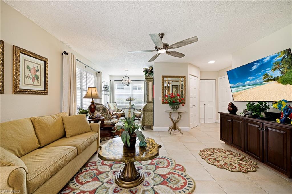 Living room with a ceiling fan, light tile patterned floors, a textured ceiling, and a chandelier