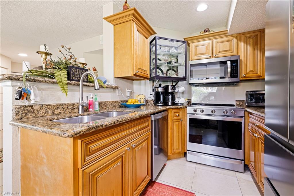 Kitchen with stainless steel appliances, a textured ceiling, stone counters, light tile patterned floors, and brown cabinetry
