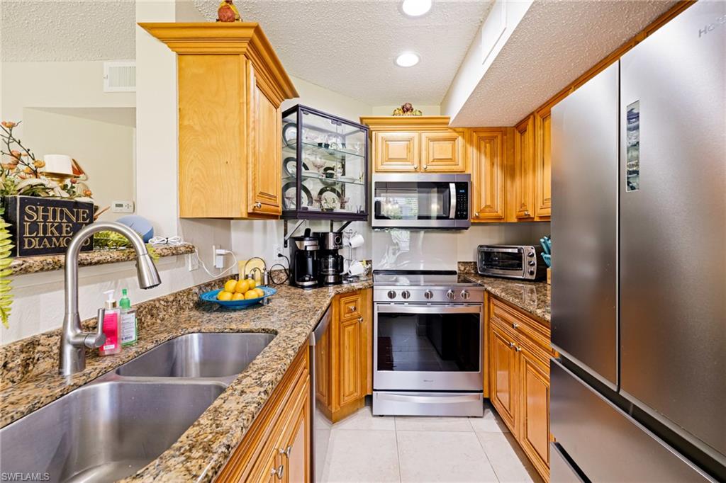 Kitchen featuring stainless steel appliances, a textured ceiling, stone counters, light tile patterned floors, and brown cabinets