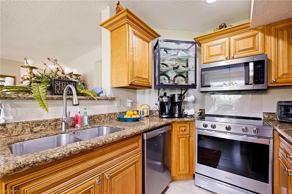 Kitchen with stainless steel appliances, a textured ceiling, stone countertops, and brown cabinetry