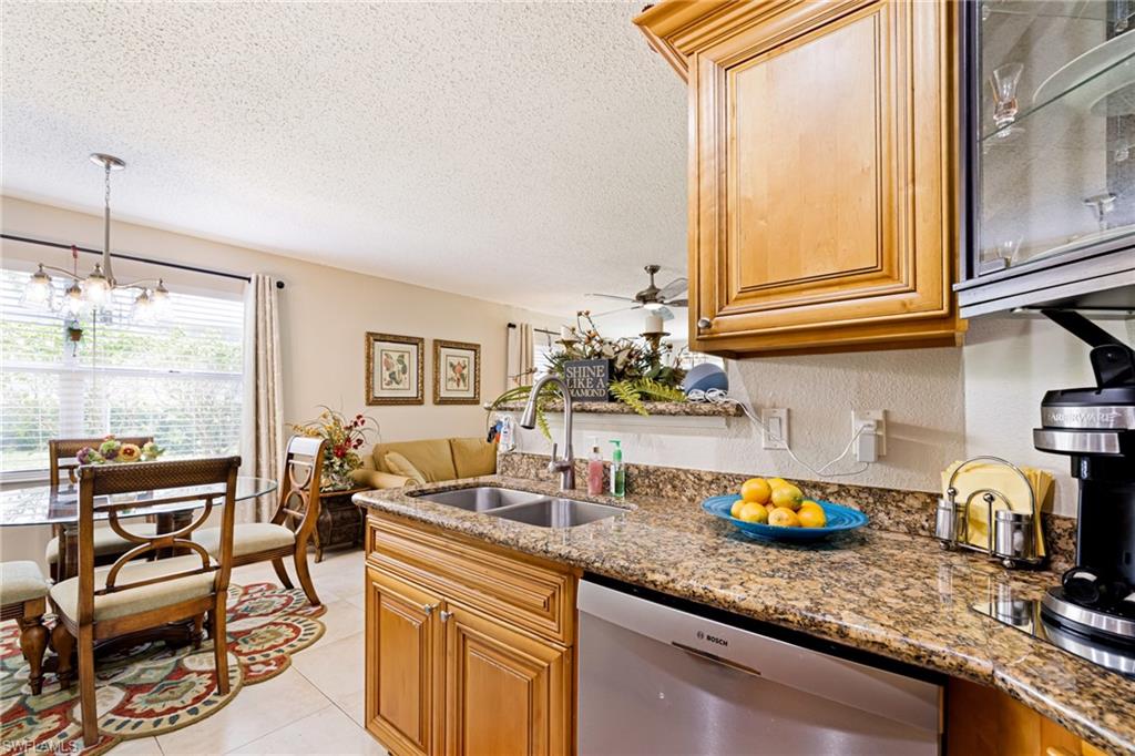 Kitchen featuring dishwasher, a textured ceiling, stone countertops, a chandelier, and a ceiling fan