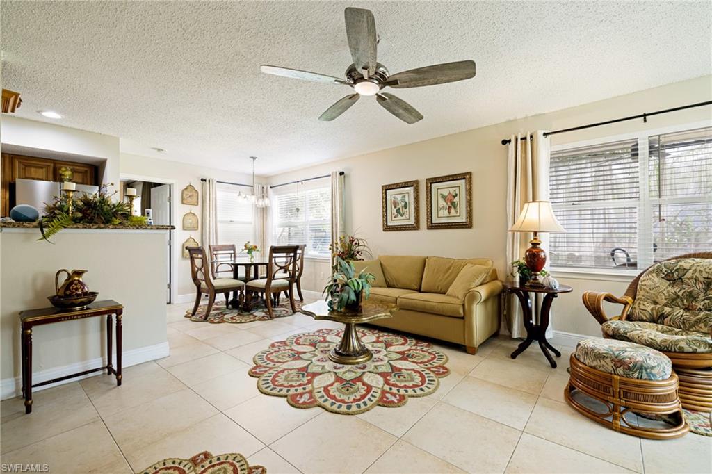 Living area featuring ceiling fan, a textured ceiling, light tile patterned floors, and a chandelier