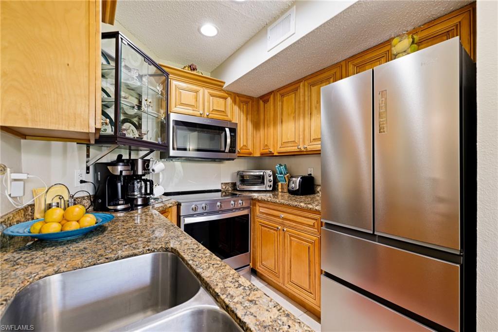 Kitchen featuring appliances with stainless steel finishes, a textured ceiling, light stone countertops, brown cabinets, and recessed lighting