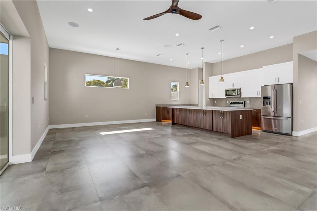 Kitchen with stainless steel appliances, white cabinets, light countertops, a large island, and ceiling fan