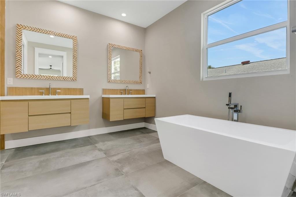 Bathroom with a freestanding bath, two vanities, concrete floors, and recessed lighting